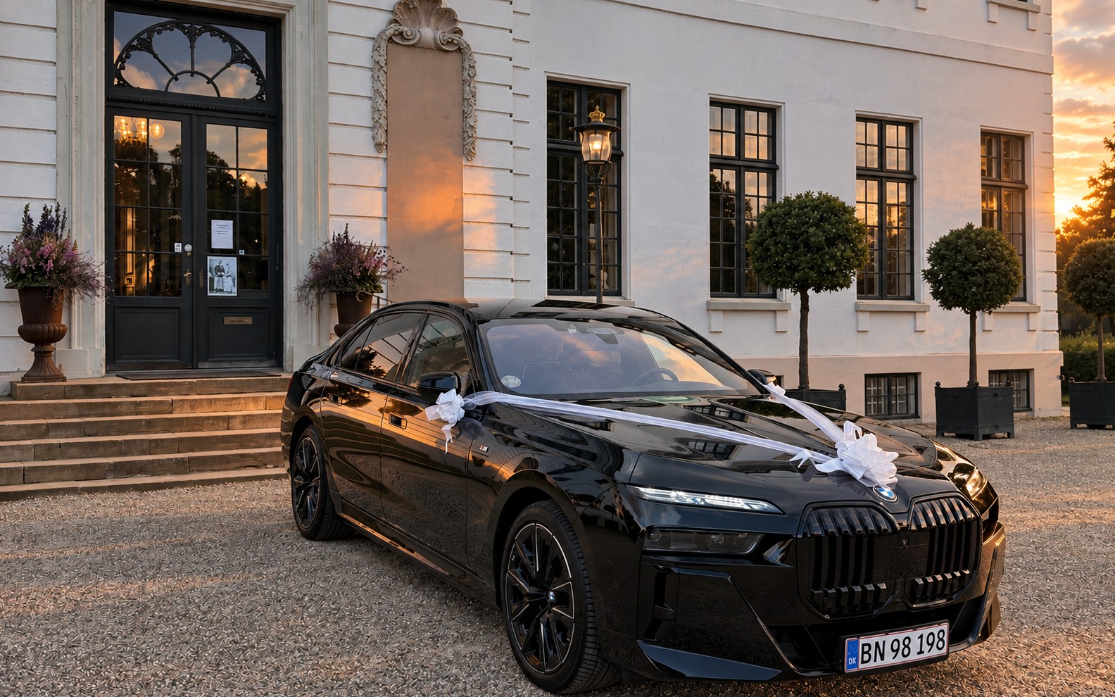 BMW i7 with white wedding ribbons outside a Danish manor house at sunset, a LuxLimo wedding car