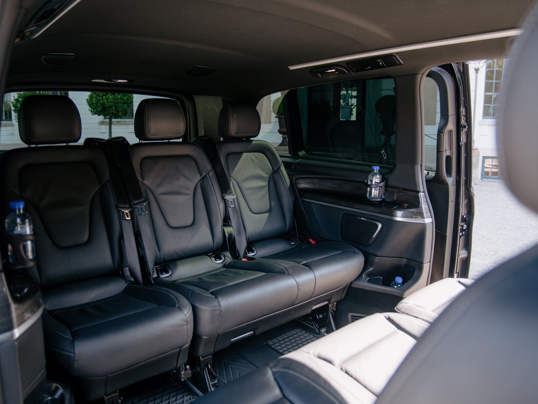 The second row of the LuxLimo Mercedes-Benz EQV seen through the open sliding door: three individual leather seats with belts and room to step in
