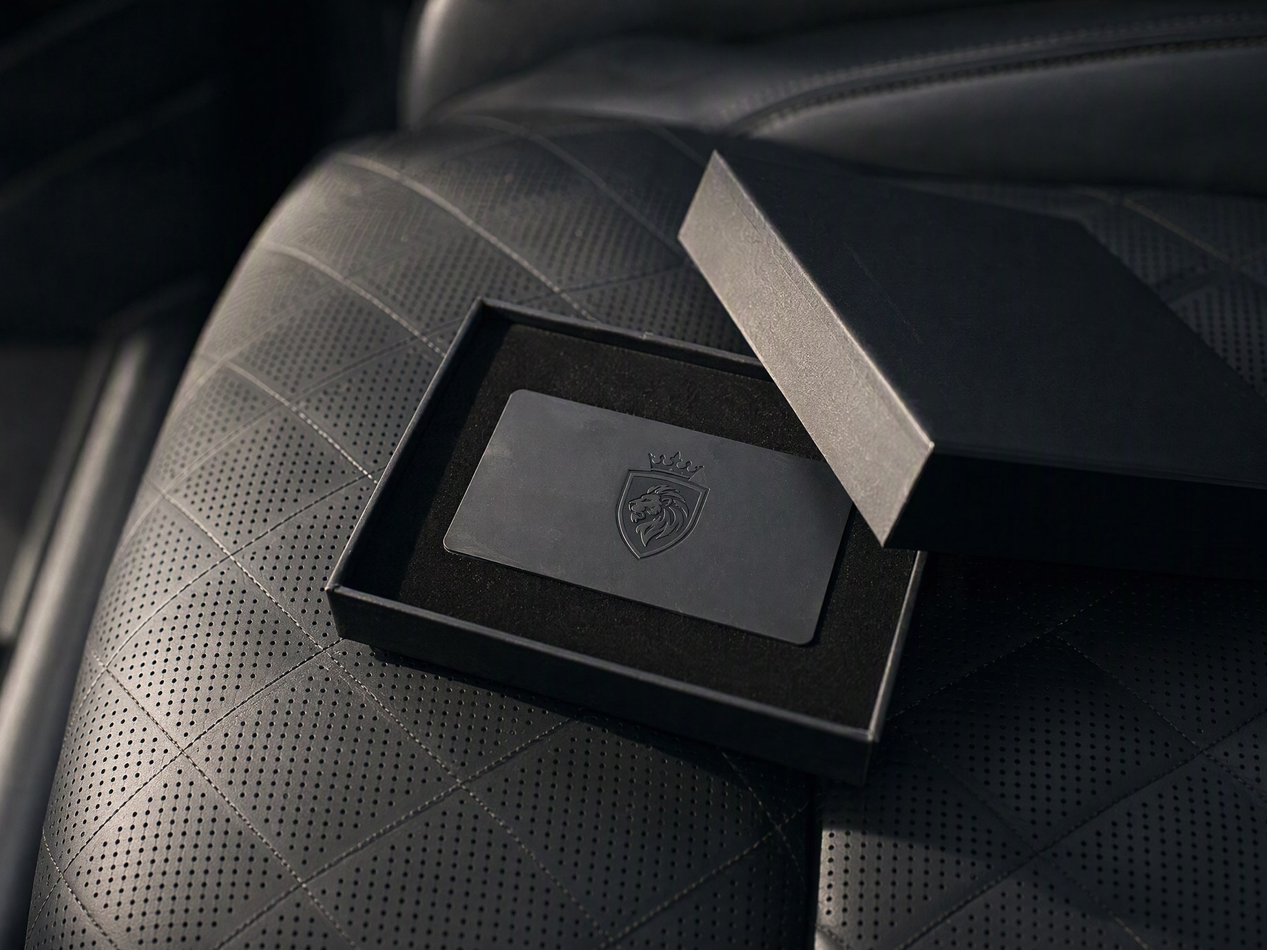 Black LuxLimo metal card with the shield logo in an open black gift box on a quilted leather rear seat