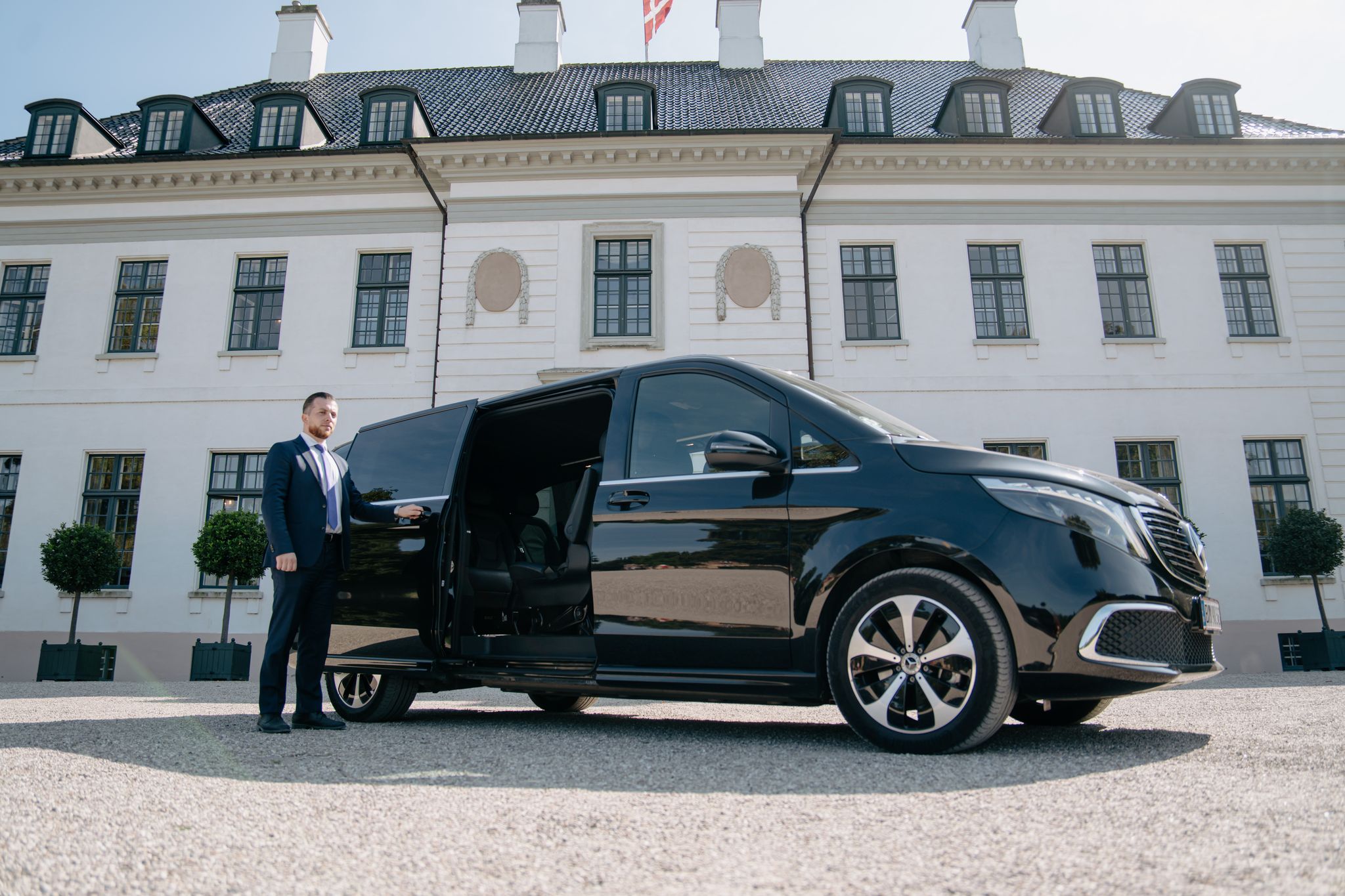 LuxLimo chauffeur holding the sliding door of the Mercedes-Benz EQV open at a Danish manor house